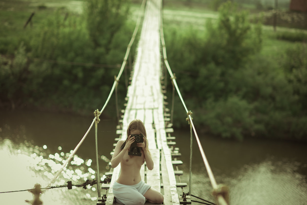 Блонда дуреет на мосту у воды голая изгибаясь как змея