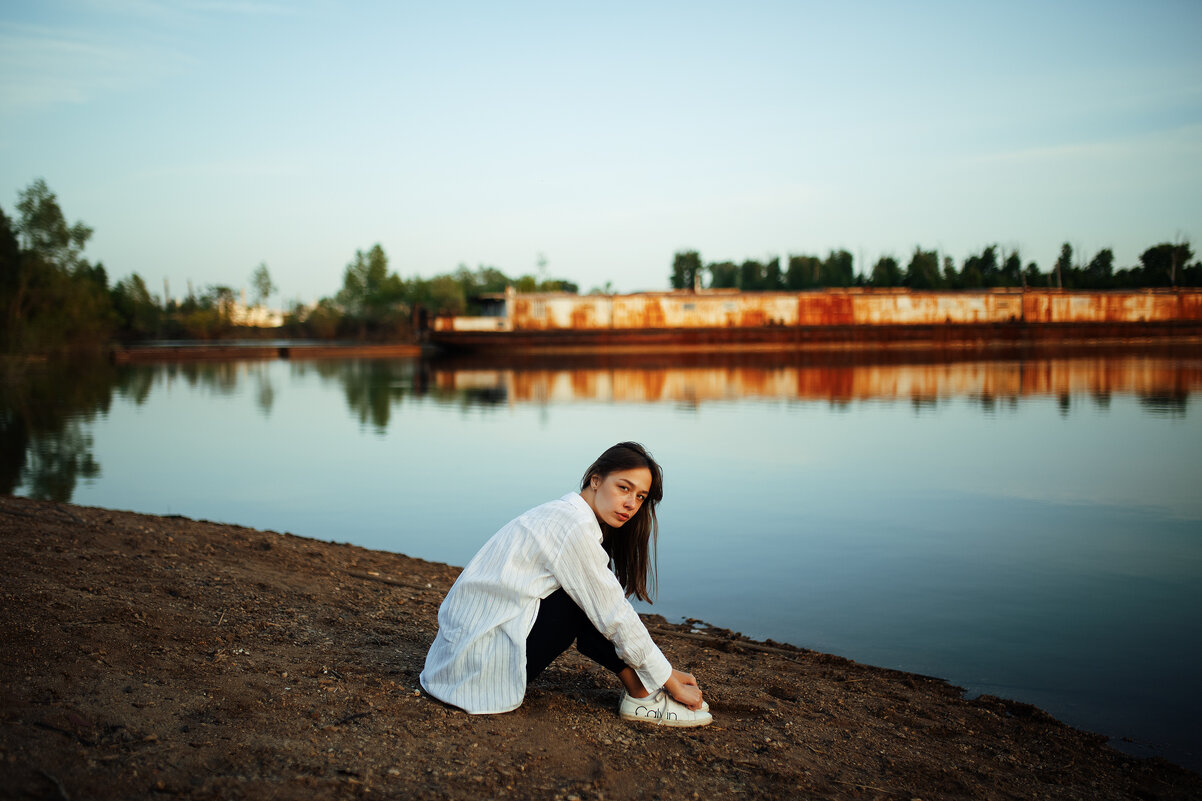 Девушка в белой рубашке сидит на берегу реки на закате на фоне корабля - Lenar Abdrakhmanov