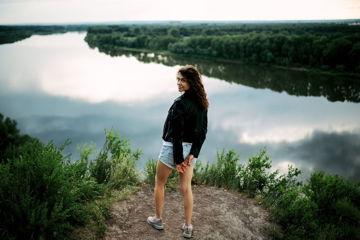 Девушка в белой футболке и кожаной куртке стоит на горе на фоне реки - Lenar Abdrakhmanov