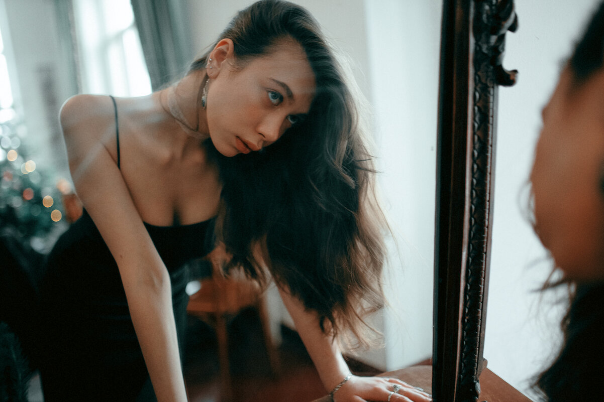 Девушка в классическом черном платье смотрит на свое отражение в зеркале - Lenar Abdrakhmanov