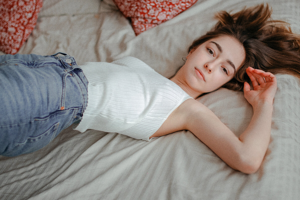 Девушка в белом топе и джинсах лежит на кровати и смотрит в камеру - Lenar Abdrakhmanov