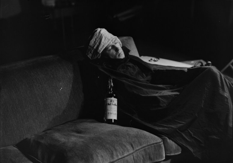 Мужчина, завернутый в одеяло, на диване с бутылкой джина, 1930-е года.